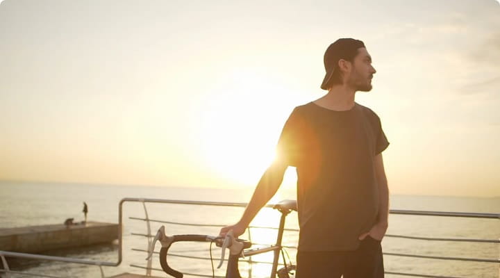 man holding his bicycle enjoying the sunset