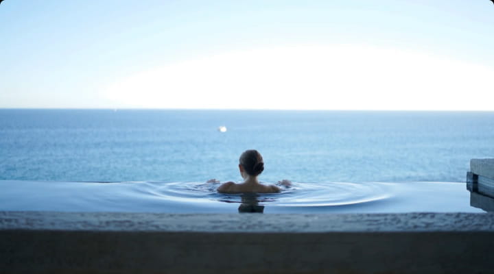 woman in a swimming pool contemplating the ocean view